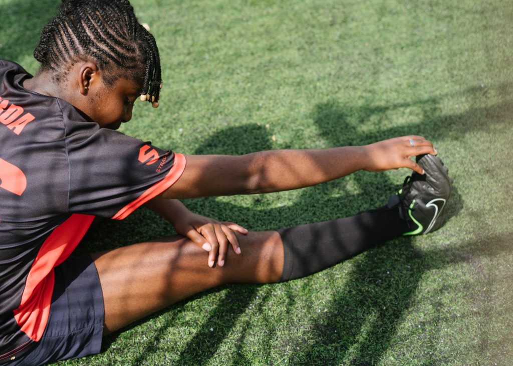 Teenage child stretching their hamstring whilst wearing a football kit
